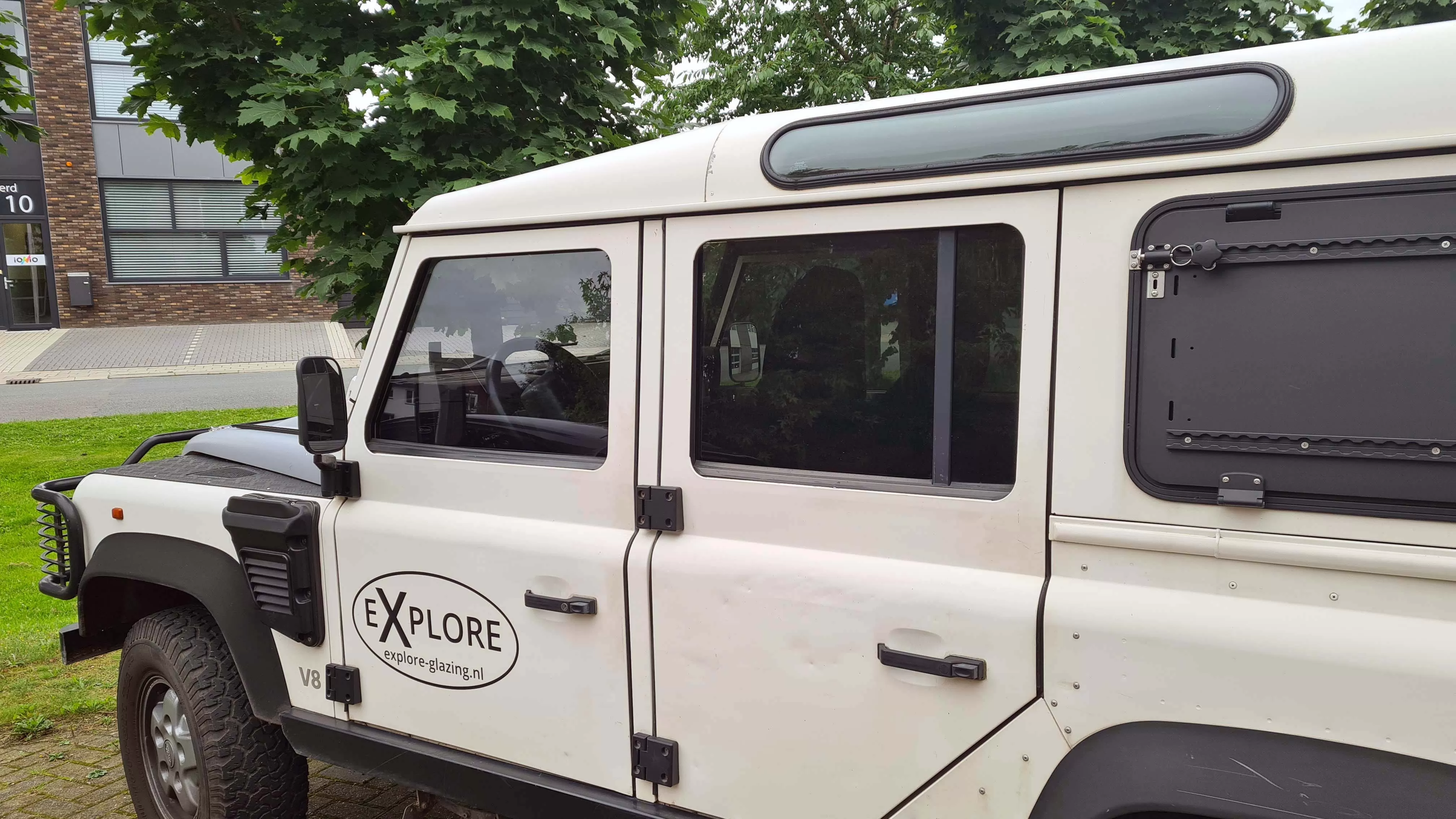 White Land Rover Defender with Explore Glazing branding and aftermarket window attachments.