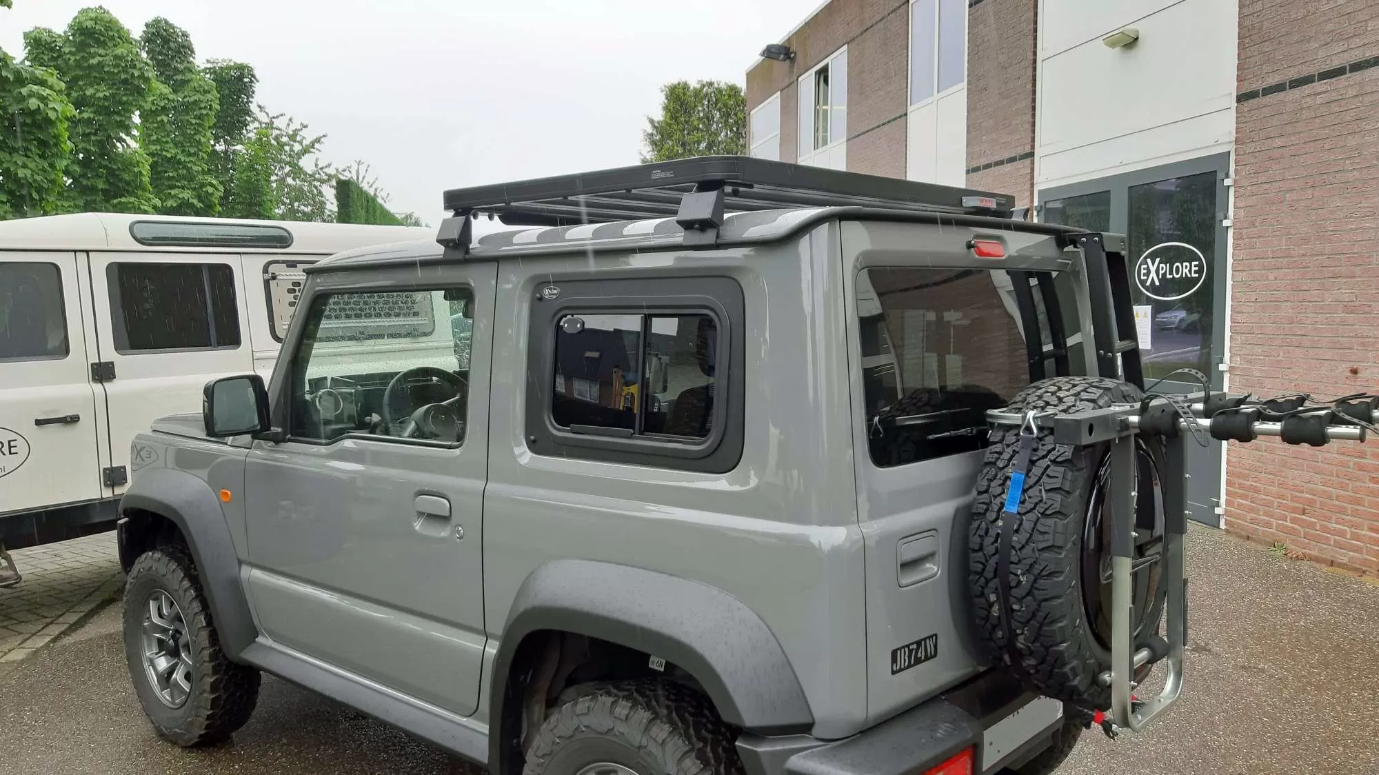 Suzuki Jimny GJ (JB74), HJ, GLX 3-door fitted with Explore Glazing sliding windows, showcasing the vehicle's rugged off-road capabilities with roof rack and spare tire mounted on the back.